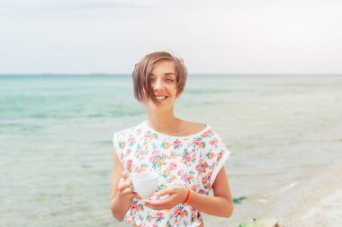 Güzel bir kadın kumsalda egzotik bir tatil sırasında dinlenir ve tatlı kahvenin tadını çıkarır.