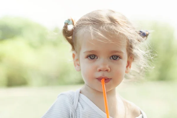 Sunny portrét malé dítě pít ze slámy juiceon rozmazané pozadí letní — Stock fotografie