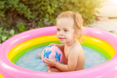 Şişme bebek havuzunda oynayan çocuk. Çocuklar yüzmek ve splash renkli yuvarlak sıcak yaz gününde su oyuncakları ile oynarken mutlu küçük kız havuz. Bahçede açık havada eğlenmek aile.