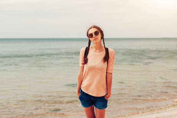 A hipster girl with braided hair in pigtails is walking along the beach in clothes. Summer concept, leisure tourism