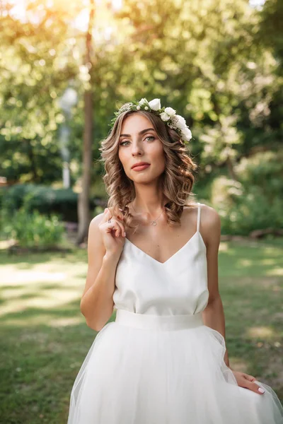 Porträt einer schönen jungen sexy Mädchen Braut mit Blumen im Haar sehen attraktiv in einem weißen Kleid auf einem Hintergrund von Sommer Natur Hintergrund posiert und lächelt — Stockfoto