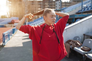 Güzel Bayan Çalıştırıcısı sıcak giysiler bir kenara seyir Stadı'nda. Kırmızı başlık giyiyor. Raslantısal spor giyim kavramı