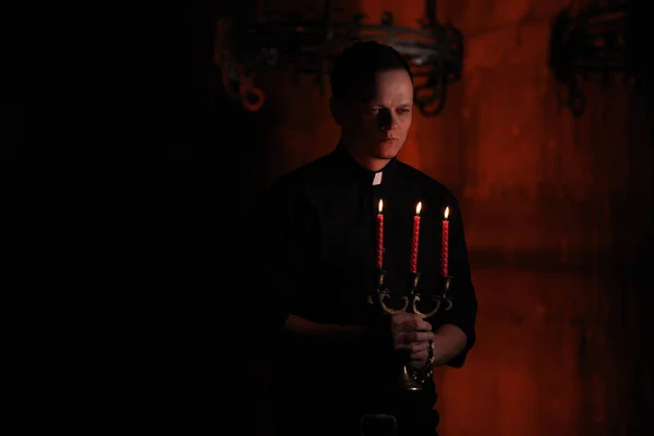 Портрет красивого католического священника или пастора с собачьим воротником, темно-красный фон. с тремя красными свечами в руке — стоковое фото
