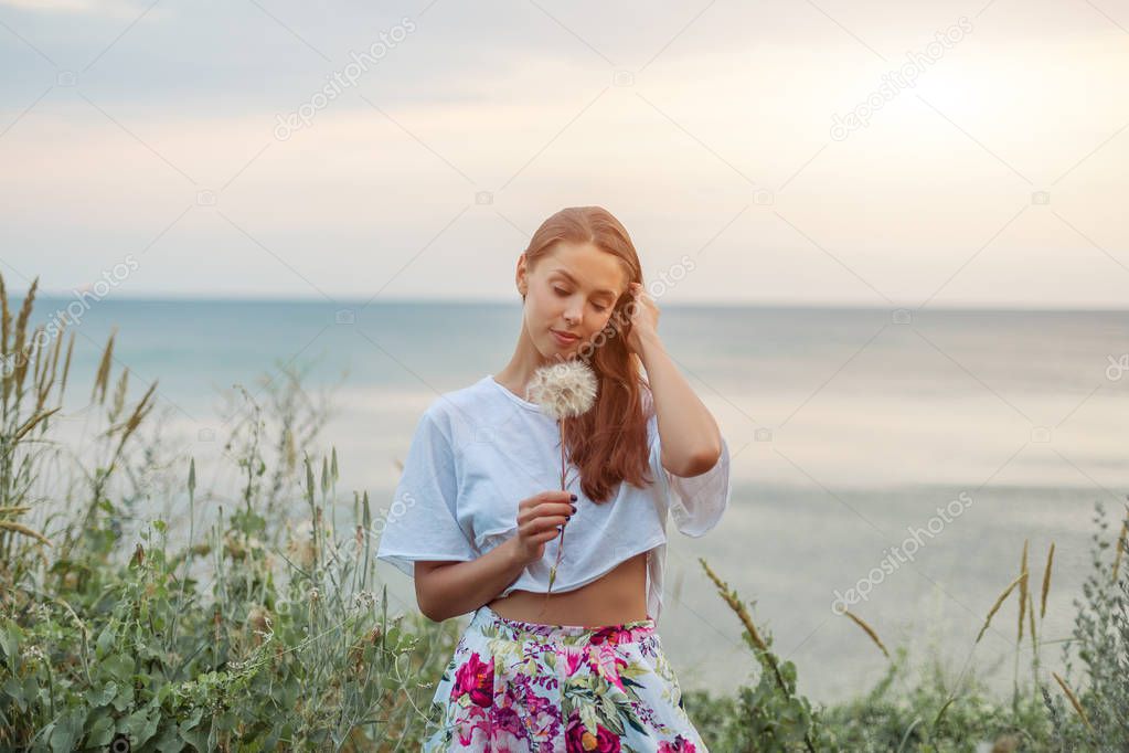 Happy beautiful woman blowing dandelion over sky and sea background, having fun and playing outdoor, teen girl enjoying nature, summer vacation and holidays, young pretty female holding flower