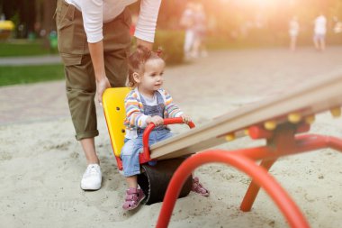 Onun bebek kız çocuklar için renkli oyun alanında oynamaktan mutlu genç annesiyle. Yaz Park'ta eğleniyor yürümeye başlayan çocuk ile anne. Bebek oyun. Yaz aile eğlence
