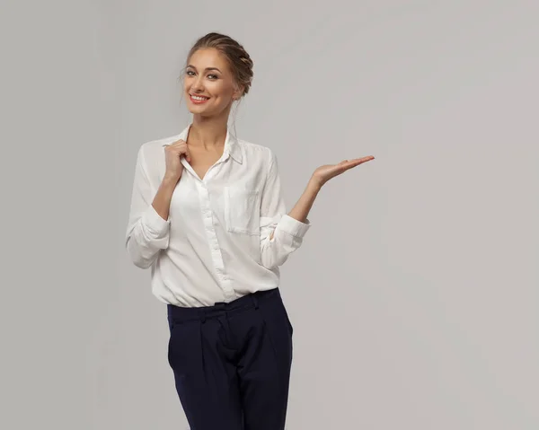 A beautiful business woman in a white classic office shirt demonstrates something on her hand with an open palm and smiles. Concept of business presentation — Stock Photo, Image