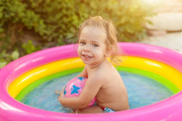 Felfújható baba medence játszó gyermekek. Gyerekek úszni, és színes kerti játék Center splash. Boldog kislány játszott játékok víz a forró nyári napon. Családi szórakozás kint a kertben. — Stock Fotó