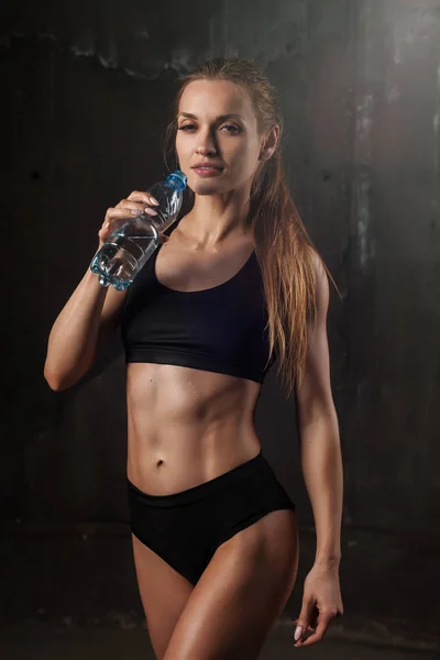 Młoda kobieta lekkoatletycznego w wodzie pitnej sprawny w studio na czarnym tle. Idealna kobieta sportowy rys. Dziewczynka fitness z idealne ciało wyrzeźbione mięśni i mocno. — Zdjęcie stockowe