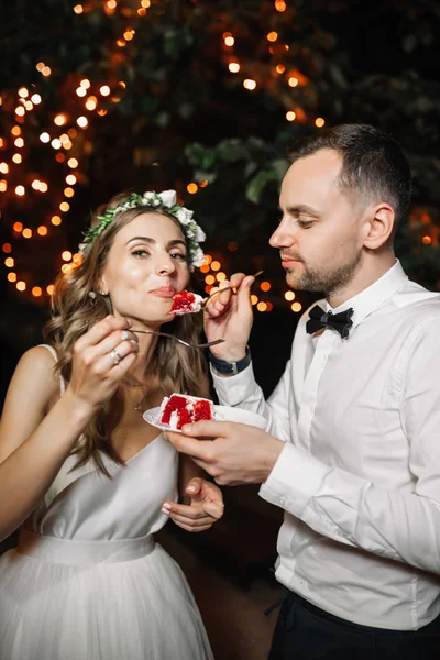 Noiva feliz e noivo cortar o bolo de casamento na decoração de luz de guirlanda frontal. Noite de casamento ao ar livre. Doce conceito de vida feliz — Fotografia de Stock