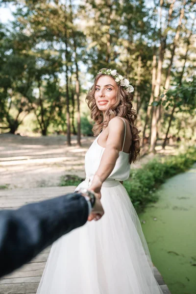 Folge mir meinem Liebeskonzept. attraktive junge Frau im weißen Hochzeitskleid hält Hand ihres Freundes und geht auf dem schönen Garten in eine glückliche Zukunft. — Stockfoto