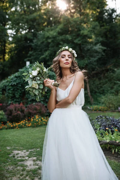 Schöne blonde glückliche Braut in elegantem weißen Kleid in einem Kranz mit Strauß im Freien — Stockfoto