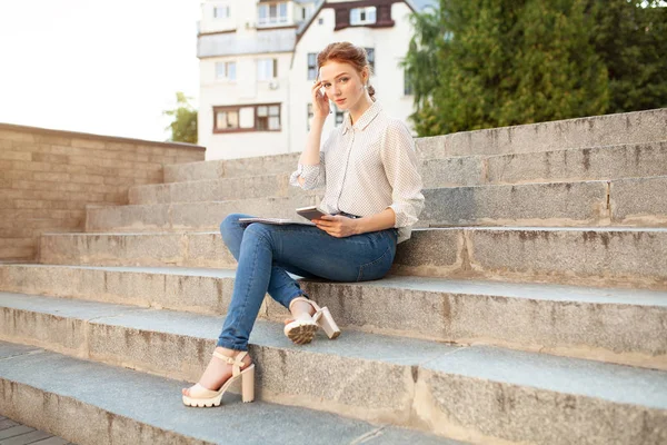 Belle jeune fille rousse avec des taches de rousseur assis sur un escalier et prendre des notes dans un carnet. Portrait d'un étudiant. Enseignement à distance. Travail à domicile — Photo