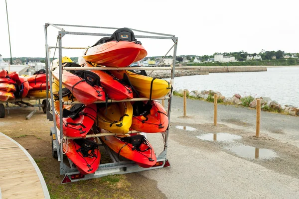 A la luz del sol, kayaks rojos, amarillos y blancos colocados boca abajo en bastidores de almacenamiento de metal. Canoa almacenada en el Brest, Francia 28 May 2018 — Foto de Stock