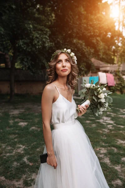 Porträt einer schönen jungen sexy Mädchen Braut mit Blumen im Haar sehen attraktiv in einem weißen Kleid auf einem Hintergrund von Sommer Natur Hintergrund posiert und lächelt — Stockfoto