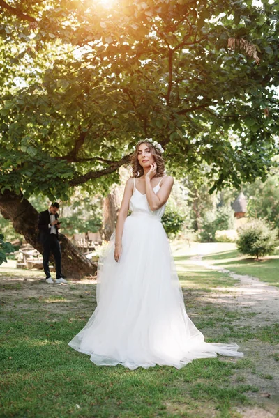 Junges Mädchen im weißen Kleid auf der Wiese. Frau in einem schönen langen Kleid posiert im Garten. atemberaubende Braut im Brautkleid — Stockfoto