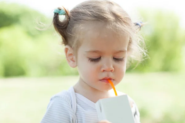 Zonnig portret van een klein kind drinken uit een rietje juiceon zomer achtergrond wazig — Stockfoto