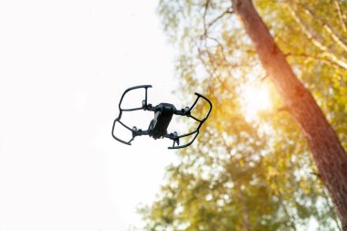 Küçük akıllı dron quadrocopter beyaz gökyüzü ve yeşil ağaçların üzerinde uçan.