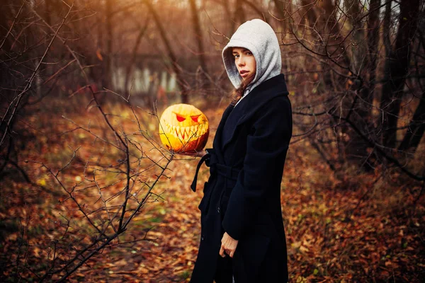 Giovane donna in un cappuccio grigio che tiene la zucca di Halloween — Foto Stock