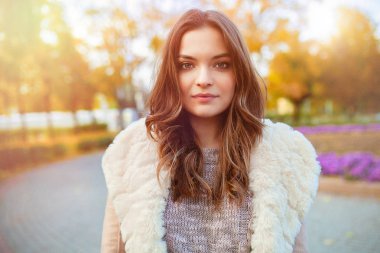 Güzel bir genç kız sonbahar parktan parlak renkli yaprakları arka plan üzerinde yürür.