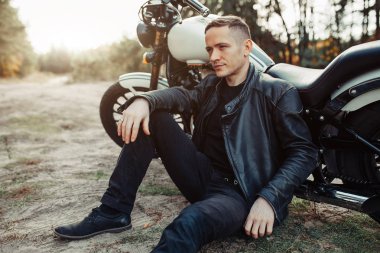 Siyah bisikletçinin ceket klasik tarzı kafe yarış motosiklet batımında yakışıklı binici adam. Bisiklet özel Vintage garajında yaptı. Acımasız eğlenceli yaşam tarzı.