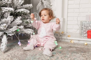 Garland ile oynarken Noel ağacı yakınındaki oturan Pembe pijama içinde küçük kız