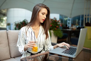 Çizgili şık elbise giymiş bir güzel kız bir yaz açık kafede oturuyor ve emrine ve arkadaşları ya sevgilisi için bekliyor. Telefonda bir ileti yazdırır