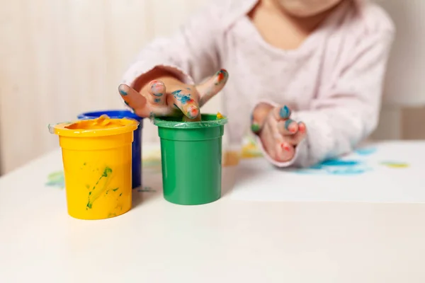 Vacker liten flicka drar med fingret färger på ett vitt papper. Kreativa barns utveckling i förskolan eller fri tid hemma — Stockfoto