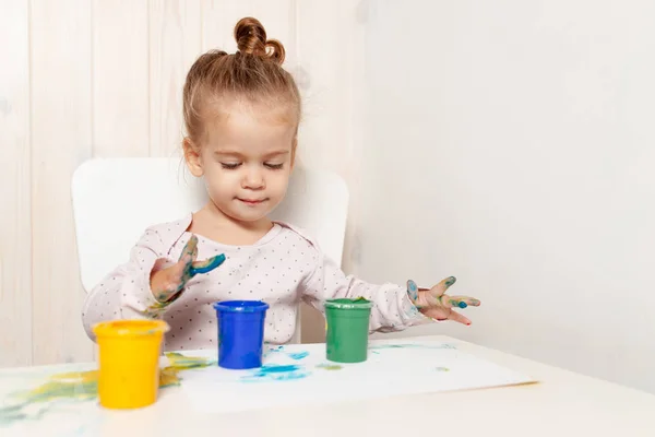 Schönes kleines Mädchen zeichnet mit Fingerfarben auf ein weißes Blatt Papier. Kreative kindliche Entwicklung im Kindergarten oder in der Freizeit zu Hause — Stockfoto