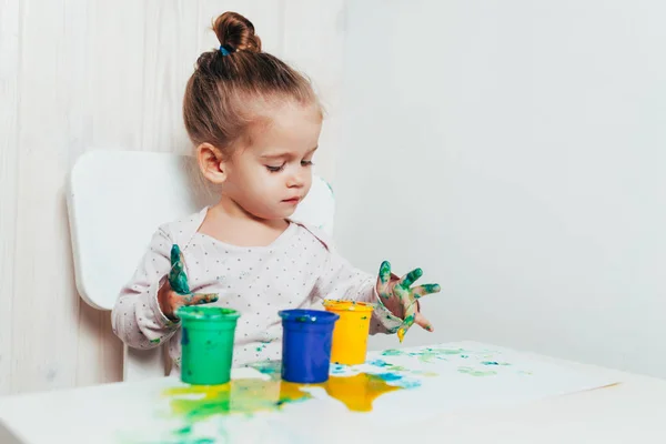 Bella bambina disegna con vernici a dita su un foglio bianco di carta. Sviluppo creativo del bambino nella scuola materna o nel tempo libero a casa — Foto Stock