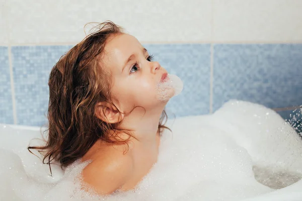 有趣的开朗快乐幼儿宝宝洗澡时玩泡沫泡泡。浴缸里的小孩微笑的孩子在浴室在蓝色背景。卫生和保健. — 图库照片