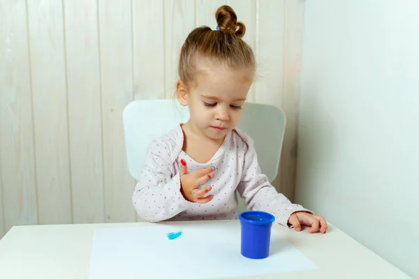 Schönes kleines Mädchen zeichnet mit Fingerfarben auf ein weißes Blatt Papier. Kreative kindliche Entwicklung im Kindergarten oder in der Freizeit zu Hause — Stockfoto