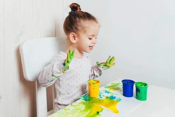 Belle petite fille dessine avec des peintures aux doigts sur une feuille blanche de papier. Développement créatif de l'enfant à la maternelle ou temps libre à la maison — Photo