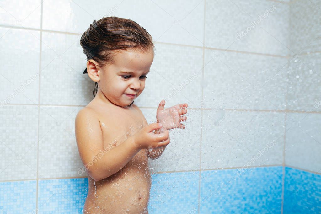 Beautiful little girl taking a bath. A child is played with water and spray from the shower. Cheerful children's hygiene. Naughty daughter in the bathroom