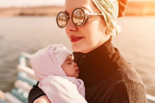 Young mother carrying her adorable baby daughter in a baby carrier on beautiful autumn park behind the lake — Stock Photo, Image