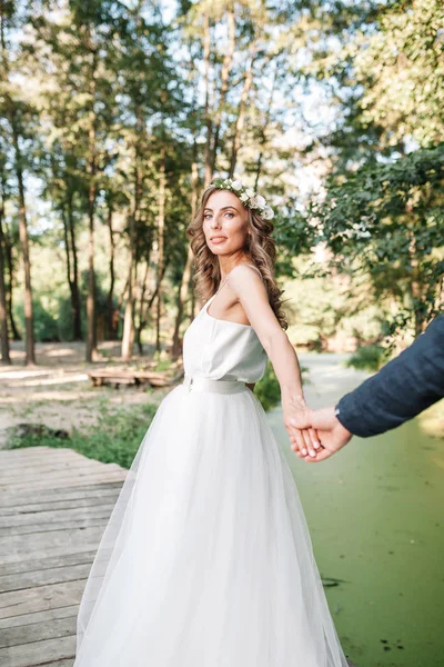 Segue-me o meu conceito de amor. Jovem atraente vestida com vestido de noiva branco segurando a mão de seu namorado e andando no belo jardim para o futuro feliz . — Fotografia de Stock