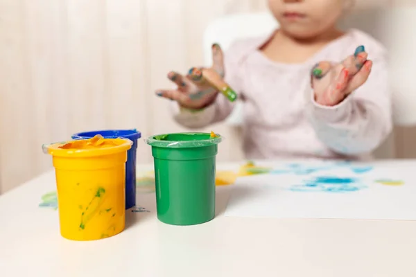 Schönes kleines Mädchen zeichnet mit Fingerfarben auf ein weißes Blatt Papier. Kreative kindliche Entwicklung im Kindergarten oder in der Freizeit zu Hause — Stockfoto