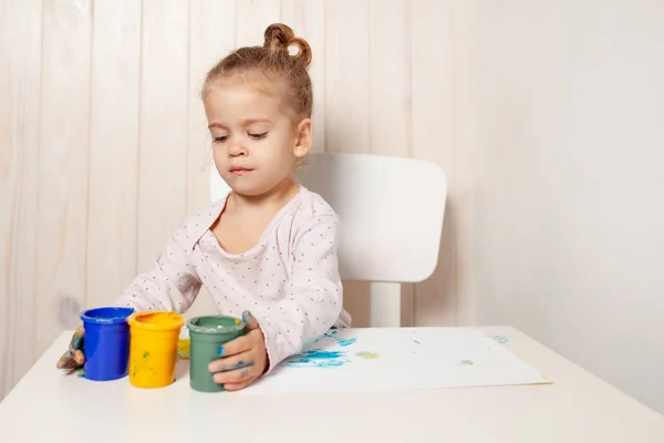 Mooi meisje tekent met de vinger de verf op een wit vel papier. De ontwikkeling van het creatieve kind in de kleuterschool of vrije tijd thuis — Stockfoto