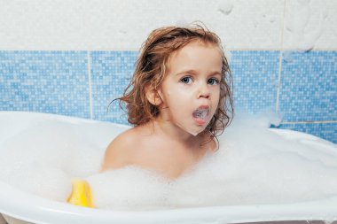 Eğlenceli neşeli mutlu toddler bebek köpük kabarcıkları ile oynarken bir banyo. Küçük çocuk bir küvet içinde. Mavi arka plan banyo çocukta gülümseyerek. Hijyen ve sağlık.