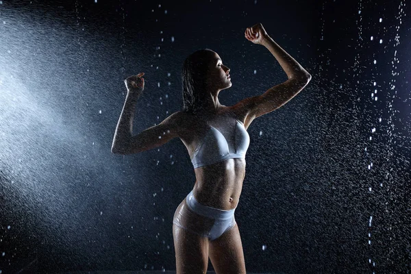 Bella ragazza in abbigliamento sportivo posa in aqua studio. Gocce d'acqua si diffondono sul suo corpo fitness. La figura perfetta sullo sfondo di spruzzi d'acqua — Foto Stock