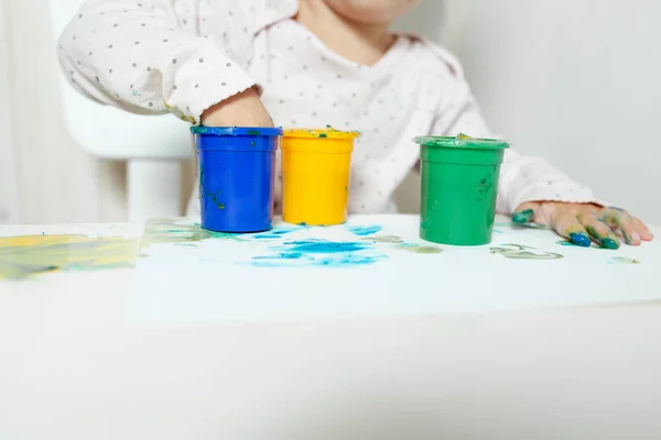Schönes kleines Mädchen zeichnet mit Fingerfarben auf ein weißes Blatt Papier. Kreative kindliche Entwicklung im Kindergarten oder in der Freizeit zu Hause — Stockfoto