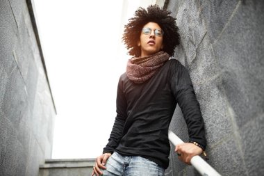 Yakışıklı genç bir saç kesimi giyimleri, kot pantolon ve bir duvar ve seramik yapılan merdiven arka planı poz bir eşarp ile karışık ırk granit fayans Afro öğrenci