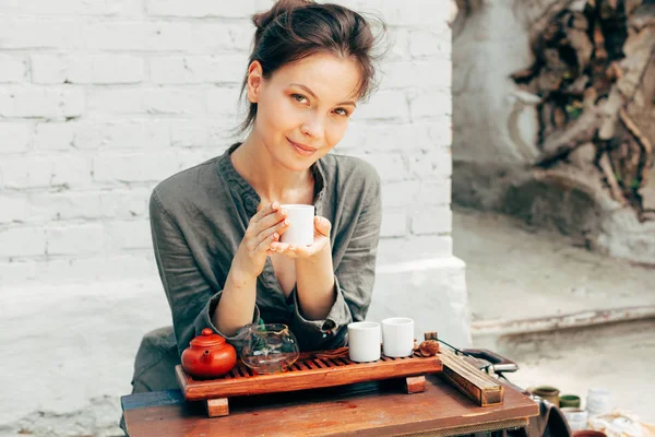 Oriental çay töreni ile arka plan üzerinde beyaz tuğla duvar ustası. Doğa gri gömlek giymiş kadın ile geleneksel çay parti — Stok fotoğraf