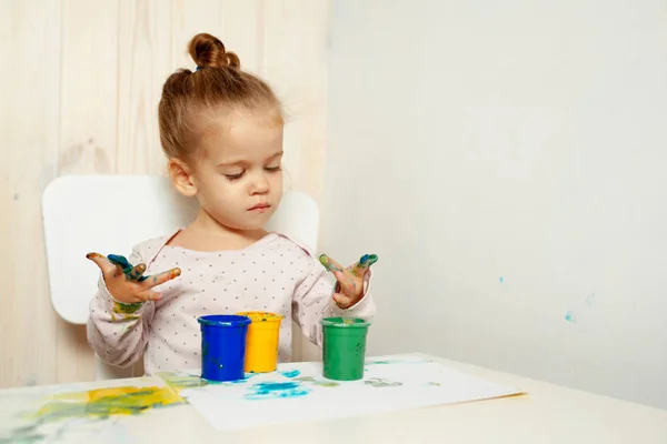A menina bonita desenha com pinturas de dedo em uma folha branca. Desenvolvimento infantil criativo no jardim de infância ou tempo livre em casa — Fotografia de Stock
