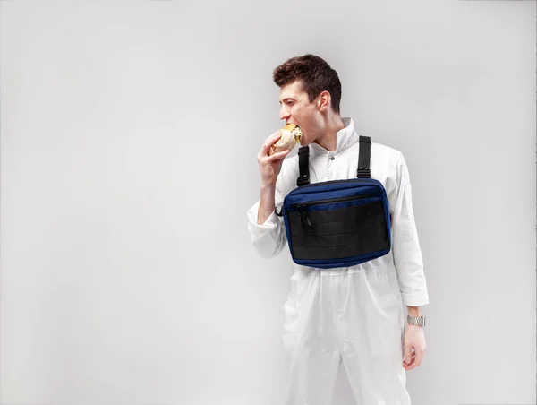 若いスタイリッシュな男性労働者リグと胸の袋には白の背景においしいジューシーなハンバーガーを食べてください。 — ストック写真