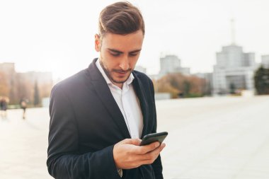 Bin yıllık iş adamı onun cep telefonu ekranına görünüyor. Yakın çekim portre. Sosyal ağlar onun smartphone içinde izlerken bir şehir sokak, Genç başarılı, şık iş adamı yürür