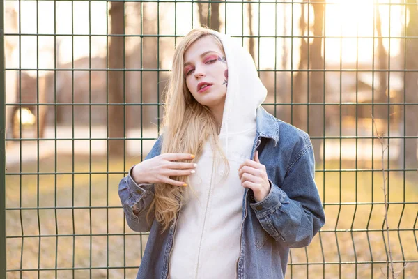 Jeune femme avec des fleurs peintes temporaires sur le visage. adolescente avec de longs cheveux blonds porter une veste de jeans et à capuche — Photo