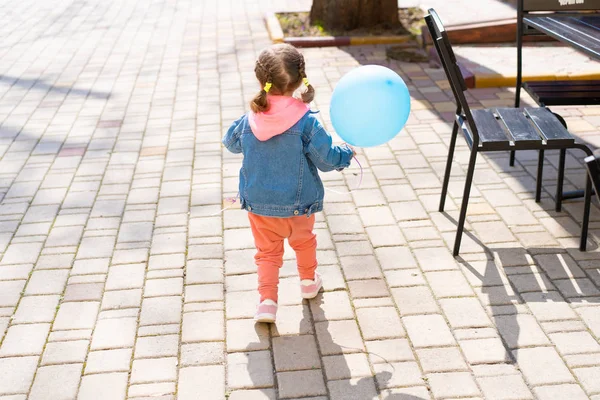 Het kleine meisje loopt weg van haar ouders met een opblaasbare bal in hun handen. — Stockfoto
