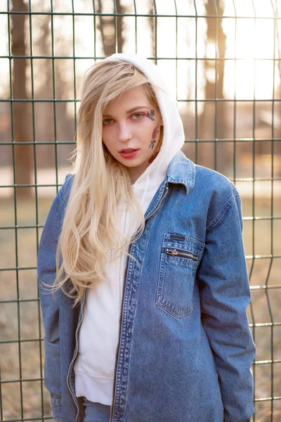 Mulher jovem com flores pintadas temporárias no rosto. adolescente com cabelo loiro longo usar jaqueta de jeans e com capuz — Fotografia de Stock