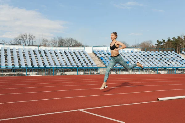 Young woman running during sunny morning on stadium track — Stock Photo, Image