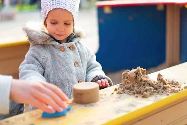 Outono. Menina fazendo figuras de areia em uma caixa de areia de crianças . — Fotografia de Stock